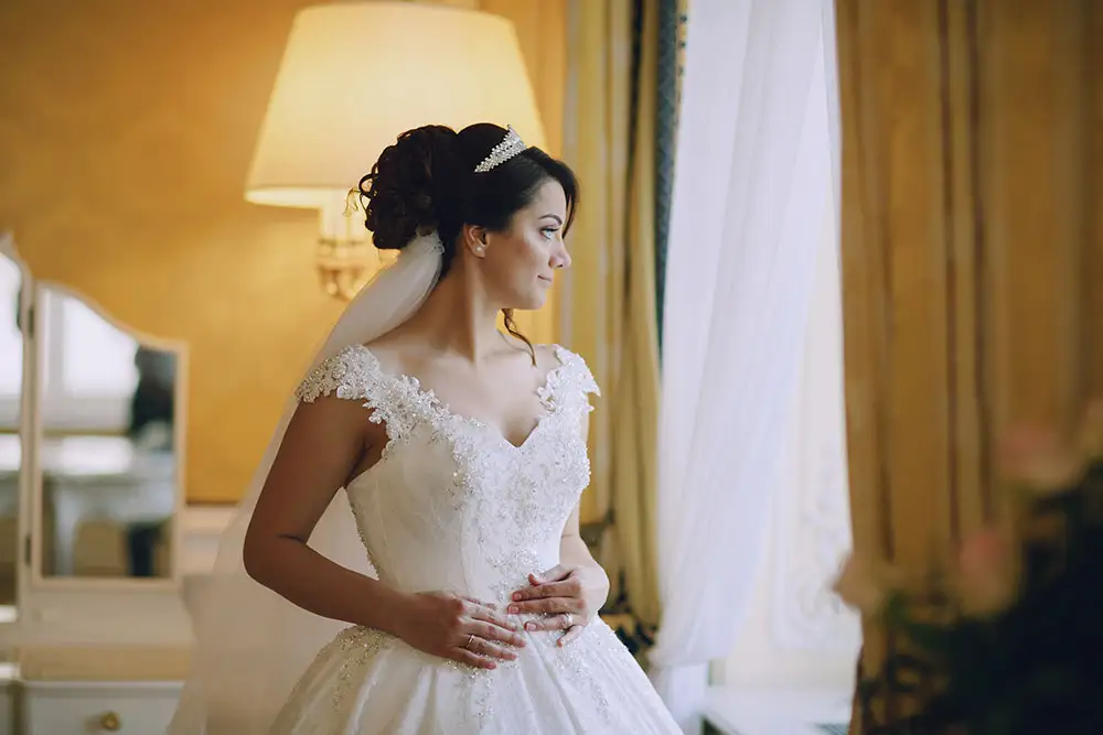 Bride with an updo and tiara standing by a window